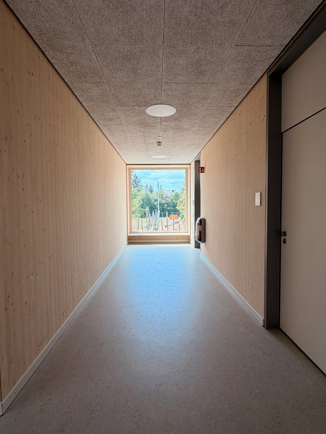 Flur aus Brettsperrholz mit bodentiefem Fenster am Ende